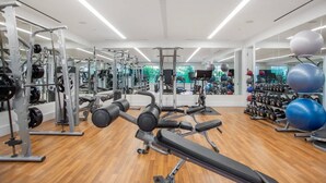 Une salle de sport moderne équipée de divers appareils d’exercice, de miroirs et dotée d’un plancher en bois.