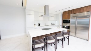 Une cuisine moderne dotée d’un îlot central, de meubles en bois, d’appareils électroménagers en acier inoxydable et d’un plan de travail blanc.