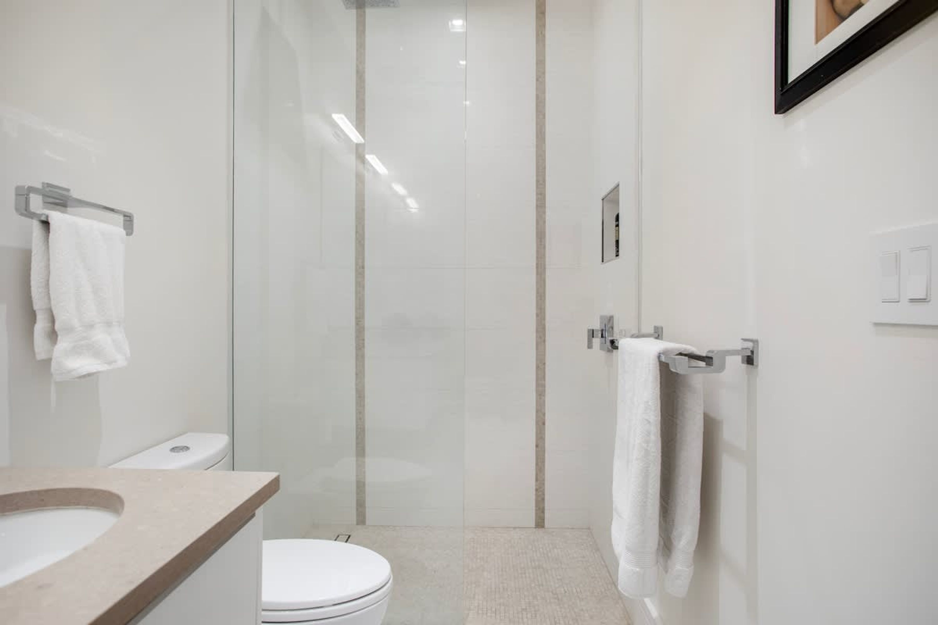 A modern bathroom with a glass shower enclosure, a toilet, and a sink with a towel rack.