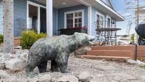 Uma estátua de urso polar em uma área de jardim, com uma casa ao fundo.