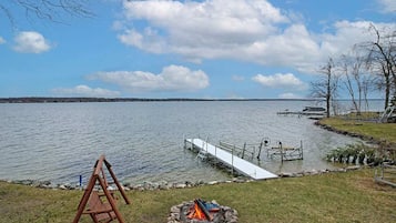 A lakeside view with a dock, a swing set, and a fire pit.