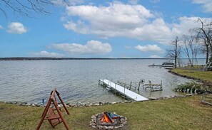 A lakeside view with a dock, a swing set, and a fire pit. - Long Lake Escape in Alpena (Alpena)