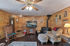 A cozy log cabin interior with a wooden staircase, a television, a fireplace, and a comfortable seating area. - Manistee Cabin in Manistee (Manistee)
