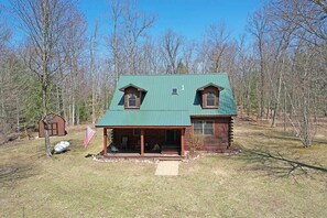 A log cabin with a green metal roof, a porch, and an American flag. - Manistee Cabin in Manistee (Manistee)