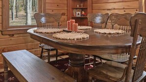 Interior de una cabaña de madera con una mesa redonda de comedor, seis sillas y un banco.