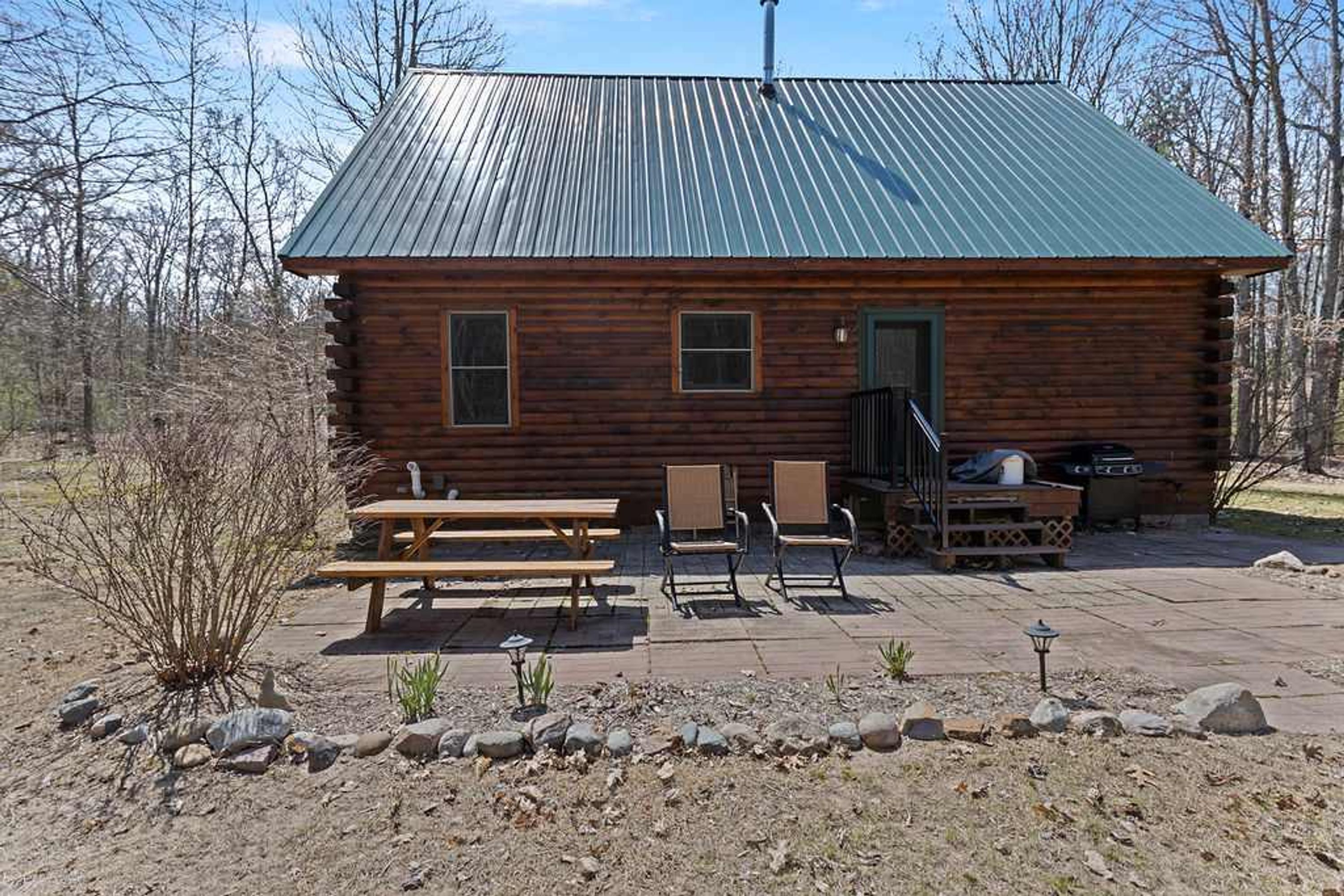 A log cabin with a metal roof, a patio with picnic tables and chairs, and a grill area.