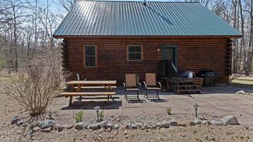 A log cabin with a metal roof, a patio with picnic tables and chairs, and a grill area.