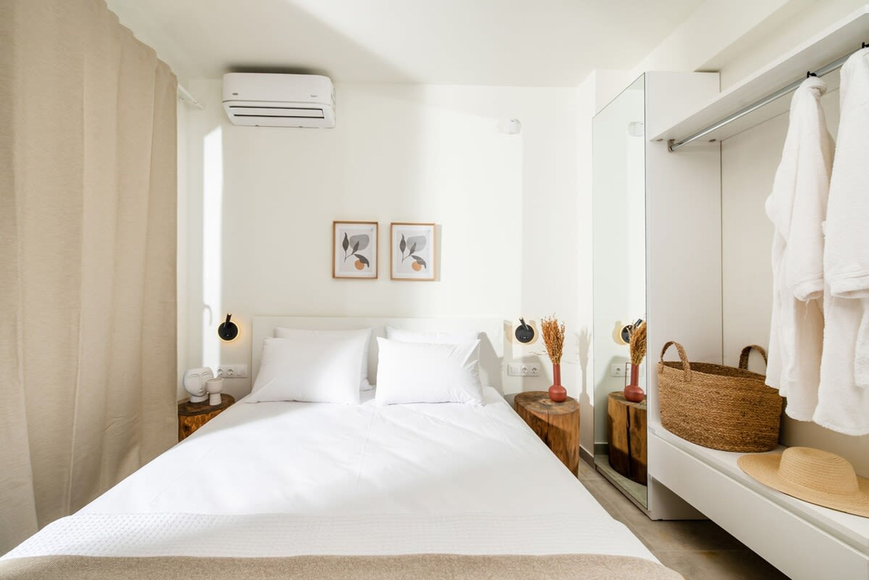 Una camera d'albergo con un letto grande, un comodino con una lampada, un condizionatore d'aria a muro e uno specchio con portasciugamani.