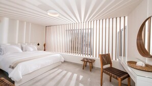 A modern bedroom with a large bed, a wooden chair, a desk, and a large window with vertical blinds.
