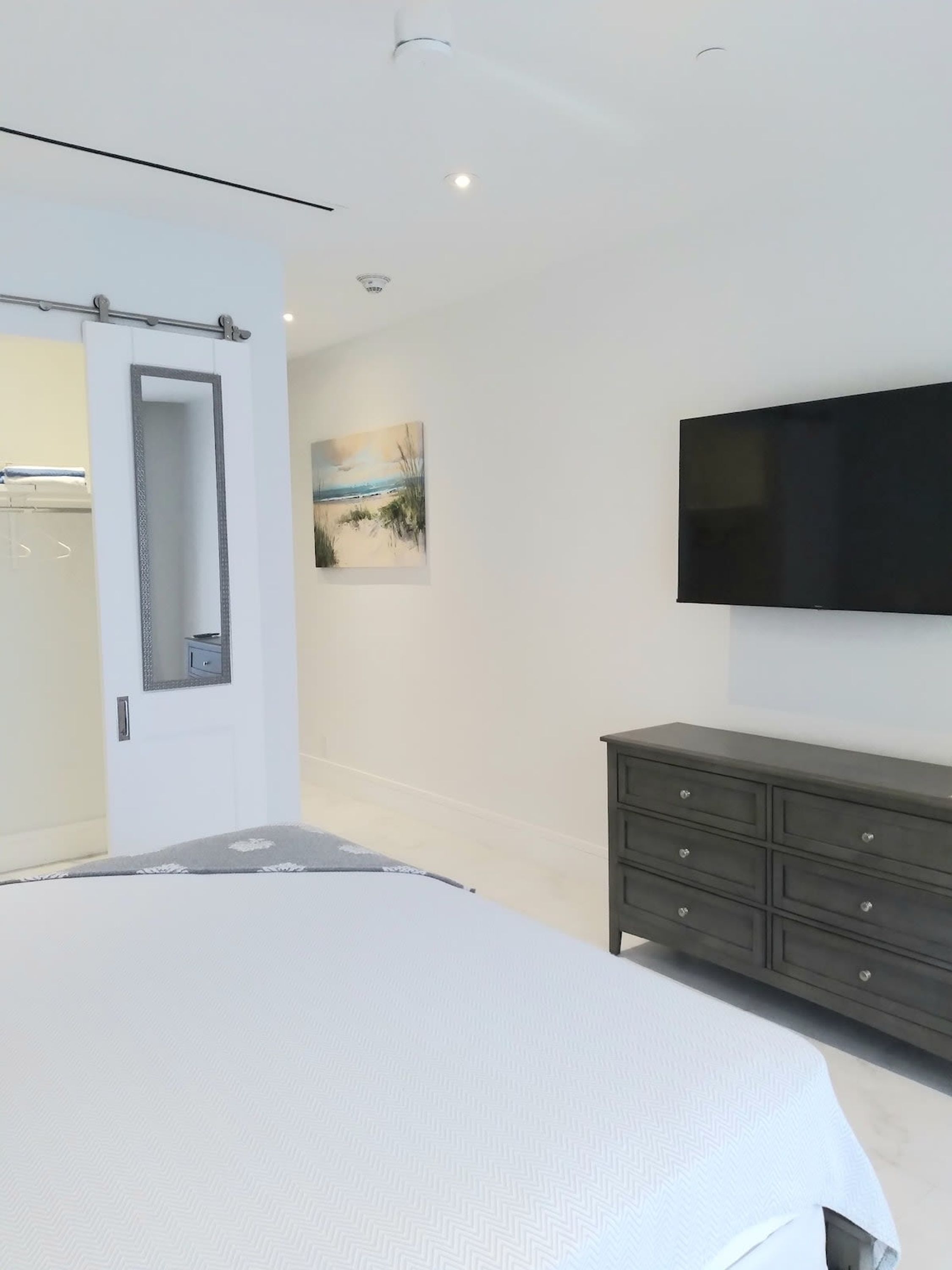 Un dormitorio con cama, tocador, televisor y un cuadro en la pared.