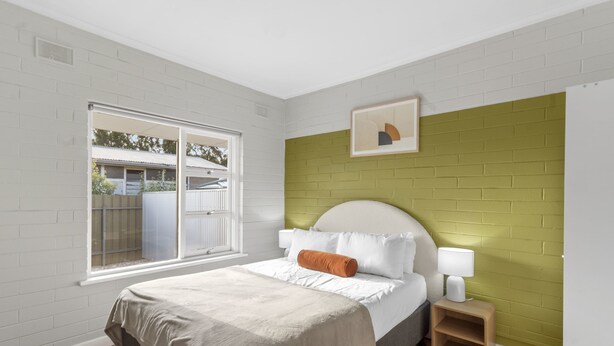 Une chambre avec un lit, une table de chevet, une fenêtre et un mur d’accent en briques vertes.