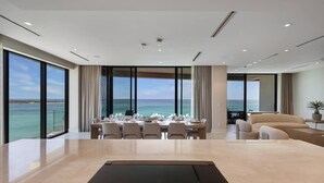 Una habitación de hotel moderna con un amplio comedor para seis personas, un sofá y vistas al océano.