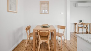Un comedor con mesa y sillas de madera, obras de arte en las paredes y una zona de cocina al fondo.
