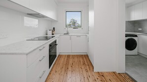 Una cocina moderna con armarios blancos, piso de madera y ventana con vista a palmeras.