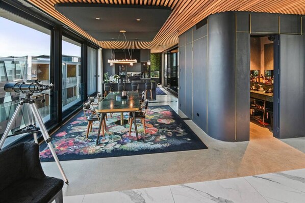 A modern dining area with a glass table, chairs, and a floral rug. - Entertainers Penthouse With 5 Bedrooms Pool spa (Auckland)