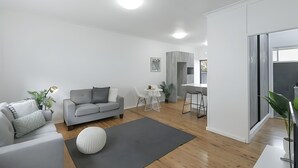 Un salon moderne avec un canapé gris, un pouf rond blanc et une petite table avec une lampe.