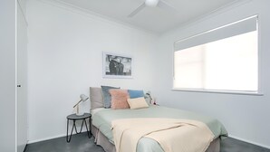 Une chambre à coucher avec un lit, une table de chevet, une lampe, un tableau au mur et une fenêtre.