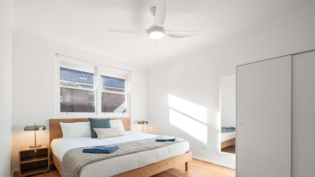 Ein modernes Schlafzimmer mit einem hölzernen Bett, einem Nachttisch, einer Nachttischlampe, einem Deckenventilator und einem Kleiderschrank.