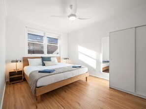 A modern bedroom with a wooden bed, a nightstand, a bedside lamp, a ceiling fan, and a wardrobe. - Prickly Pear Stays in Mayfield West (Newcastle)
