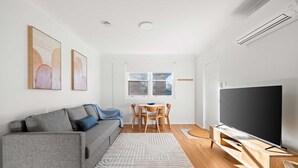 Ein modernes Wohnzimmer mit einem grauen Sofa, einem Flachbildfernseher, einem Holzesstisch und einem großen Fenster.