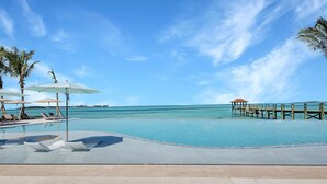 A pool area with lounge chairs and umbrellas, a wooden pier extending into the water, and a clear blue sky.
