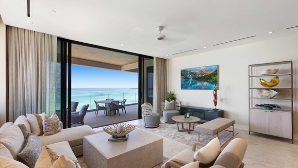 A modern living room with a large sofa, a coffee table, and a view of the ocean. There is a dining area with chairs and a table, and a painting on the wall.
