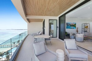 A balcony with a view of the ocean, furnished with white wicker chairs and a round table.