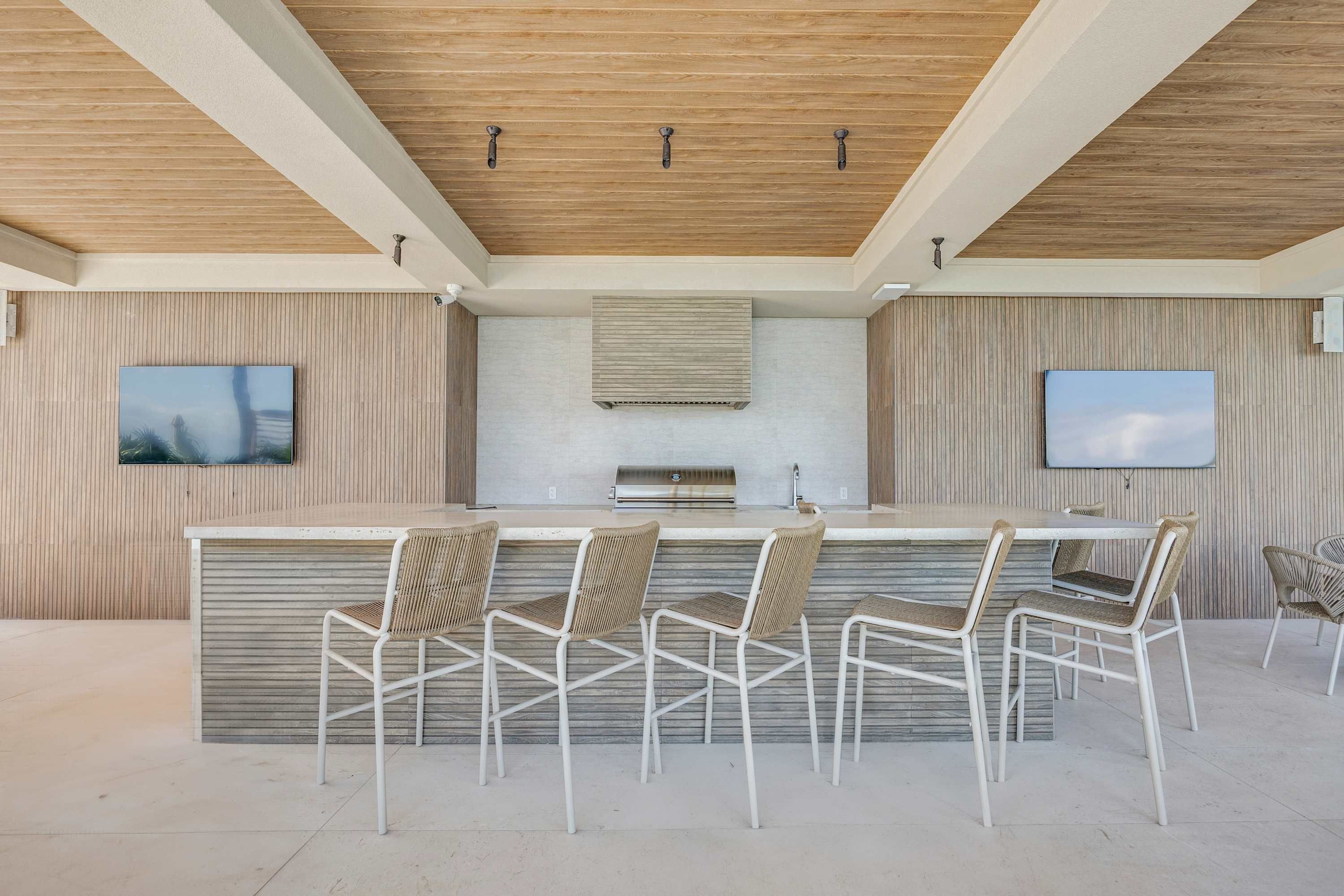 A modern outdoor kitchen with a bar area, seating, and a TV mounted on the wall.
