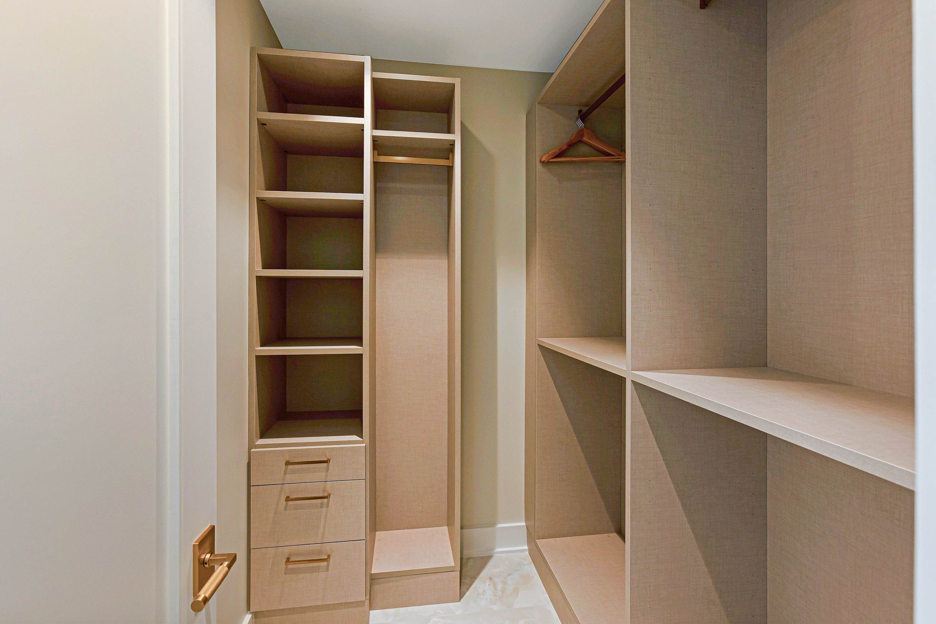 Un vestidor con amplias repisas y cajones, una barra para colgar ropa y una puerta con pomo dorado.