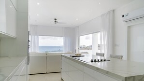 A modern kitchen with a large island, white cabinetry, and a view of the sea. - Lilypad Luxurious Cliffside Villa With Stunning Sea Views (Ocean City)