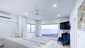 A modern bedroom with a large bed, a TV, and a view of the ocean. - Lilypad Luxurious Cliffside Villa With Stunning Sea Views (Ocean City)