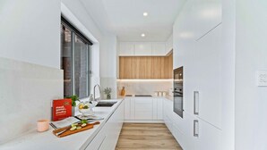 A modern kitchen with white cabinetry, a wooden floor, and a window. - Phoenix Apartment at Palm View Collective (Sydney)