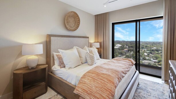 Un dormitorio moderno con una cama grande, una mesita de noche, un ventilador de techo y vistas a la ciudad a través de un ventanal.