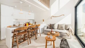 A modern kitchen with white cabinets, wooden chairs, and pendant lights.
