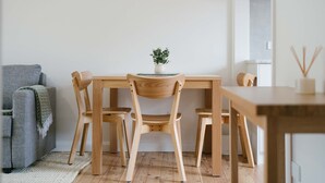 Un coin repas minimaliste avec une table et des chaises en bois, une petite plante en pot et un canapé gris.