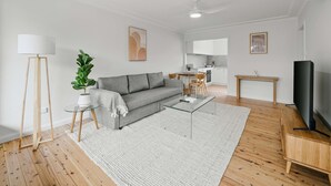 Un salon moderne avec un canapé gris, une table basse en verre, un plancher en bois et un téléviseur à écran plat.