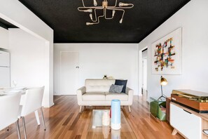 Uma sala de estar moderna com piso de madeira, um sofá branco, uma mesa de centro de vidro e um lustre.