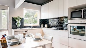 A modern kitchen with white cabinetry, a dining table set for four, and a large window providing natural light. - Renovated Retro Apartment Near Harbour Front Walks (Sydney)