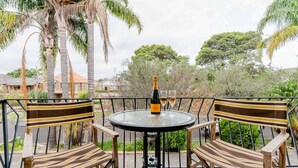A round table with two striped chairs, a bottle of champagne, and two glasses on a balcony with a view of trees and houses. - Renovated Retro Apartment Near Harbour Front Walks (Sydney)