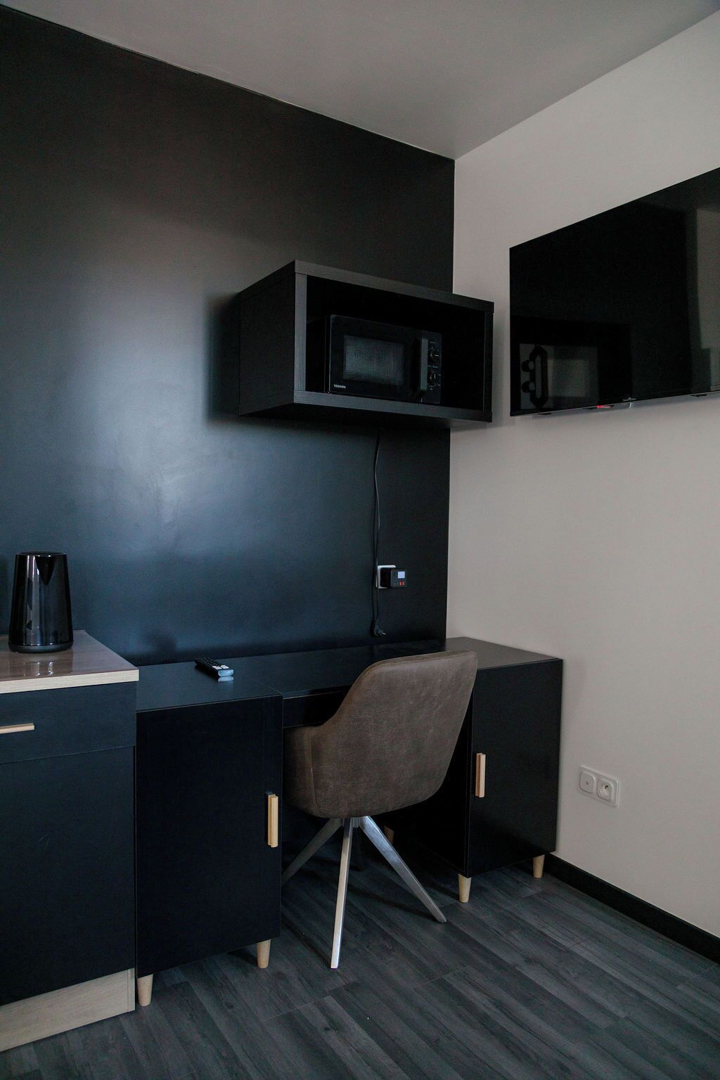 A modern office space with a desk, chair, and mounted microwave.