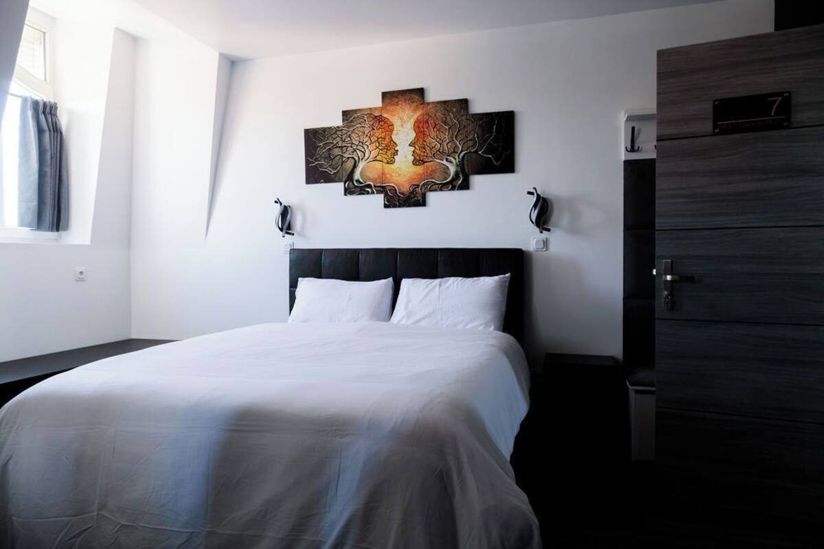Een moderne slaapkamer met een groot bed, een donkere houten dressoir en een aan de muur bevestigd kunstwerk.