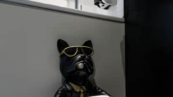 Un baño con un dispensador de papel higiénico con forma de perro de gafas de sol, una toalla colgada en la pared y un dispensador de papel.