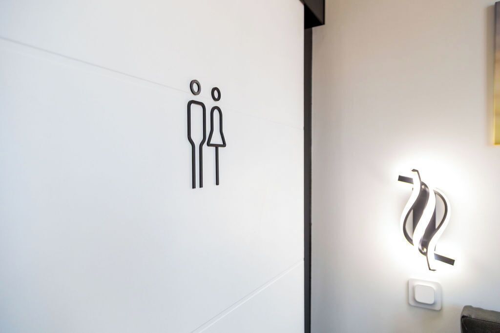Letrero de baño minimalista con un símbolo de género y una lámpara moderna.