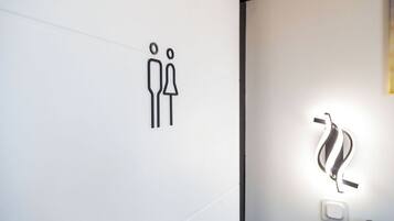 Letrero de baño minimalista con un símbolo de género y una lámpara moderna.