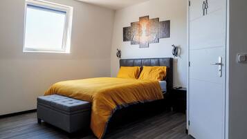A bedroom with a bed, a window, a door, and a wall-mounted artwork.