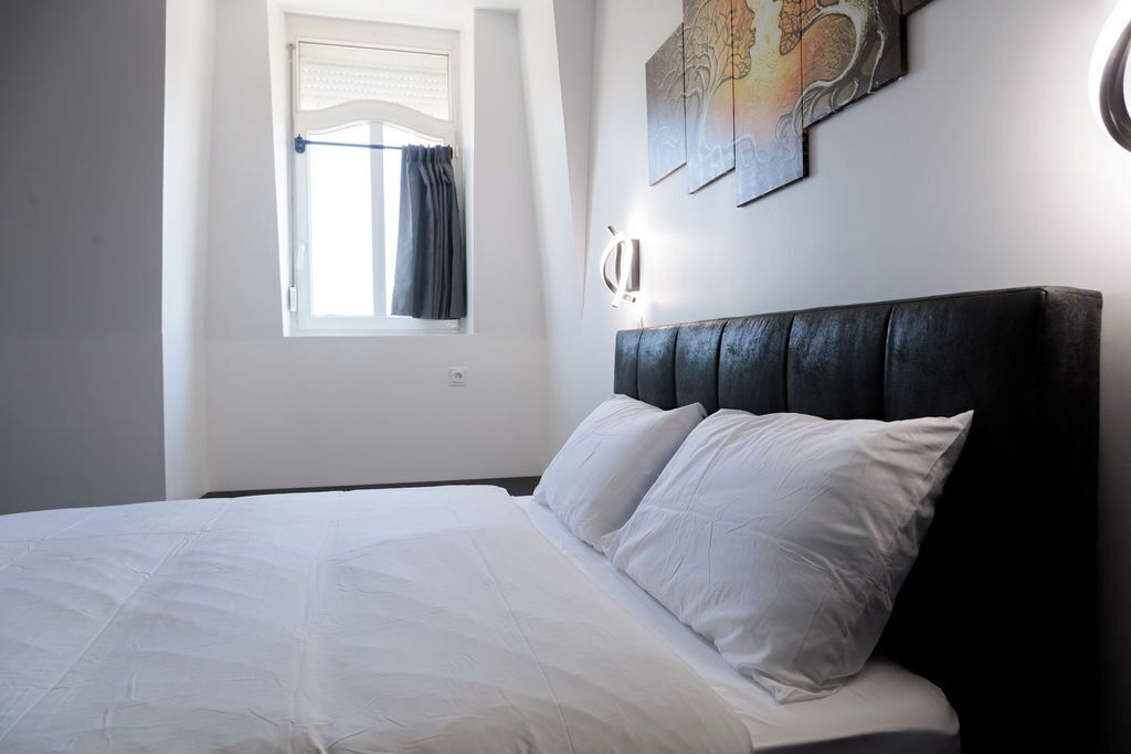 Ein Schlafzimmer mit Bett, einem Fenster mit Vorhängen und einer Wandleuchte.