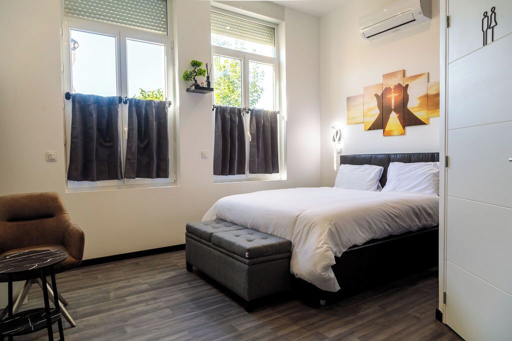 A bedroom with a bed, a chair, a small table, and a window with curtains.