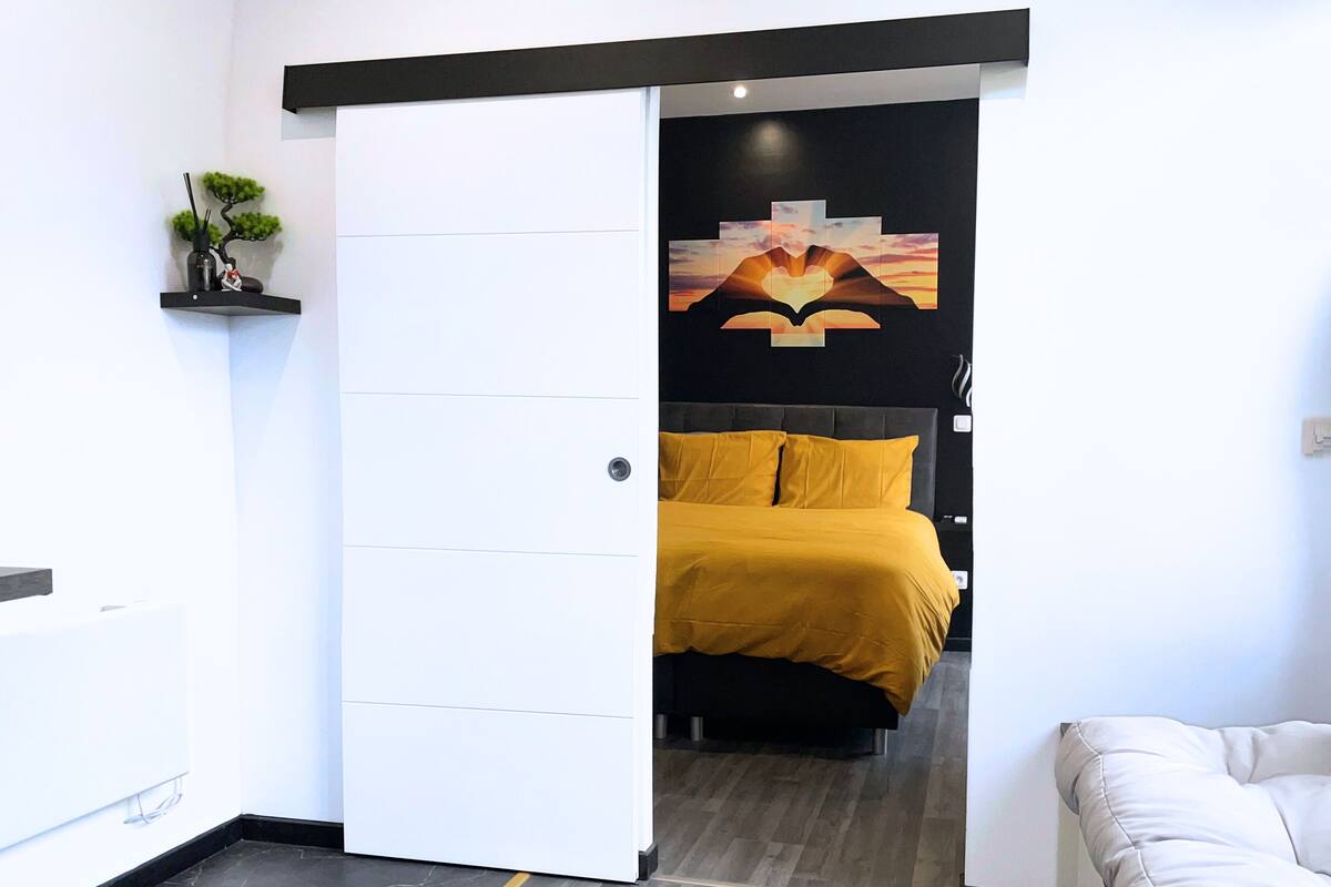 Een moderne slaapkamer met een bed, nachtkastje, een wandplank met een plant en een schilderij boven het bed.