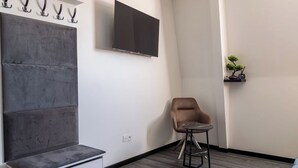 A modern room with a grey sectional sofa, a flat-screen TV mounted on the wall, a small round table, and a potted plant on a shelf. - SEE - Gare de Marly (Valenciennes)