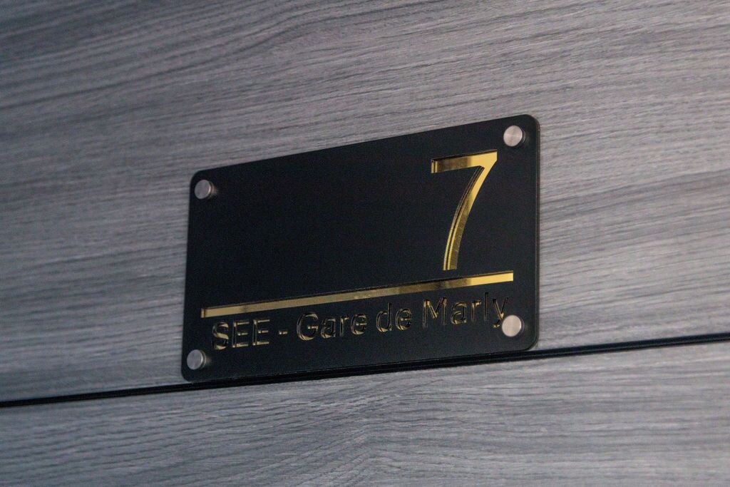A black metal plaque with the number 7 and the text "SEE - Gare de Marly".